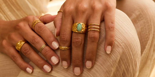 Manos con anillos bañados en oro de San Saru: anillo martillado con piedra verde, anillos espiral y alianzas finas apiladas